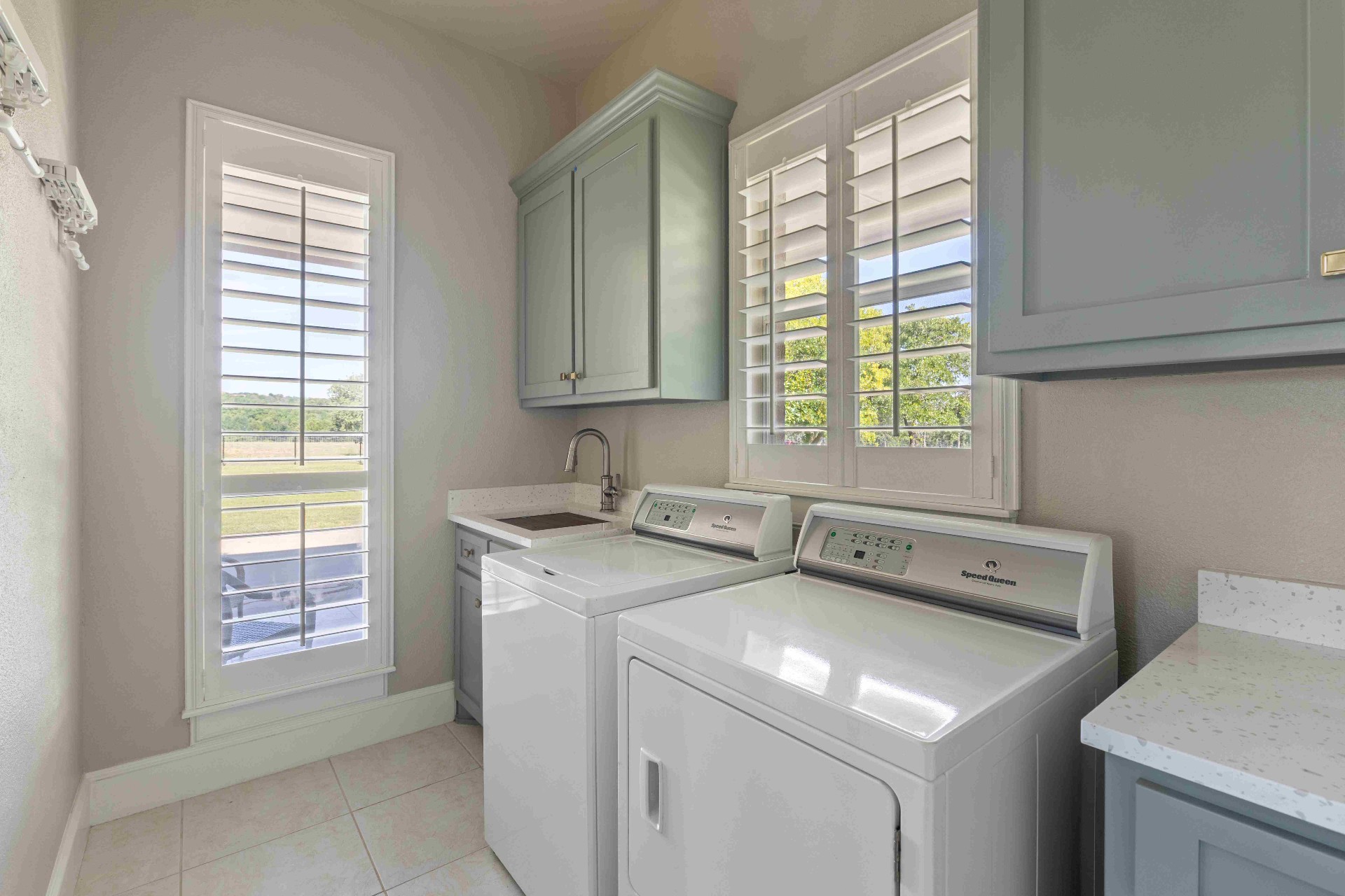 Laundry room with sage cabinetry, quartz counters, utility sink, and Speed Queen washer and dryer