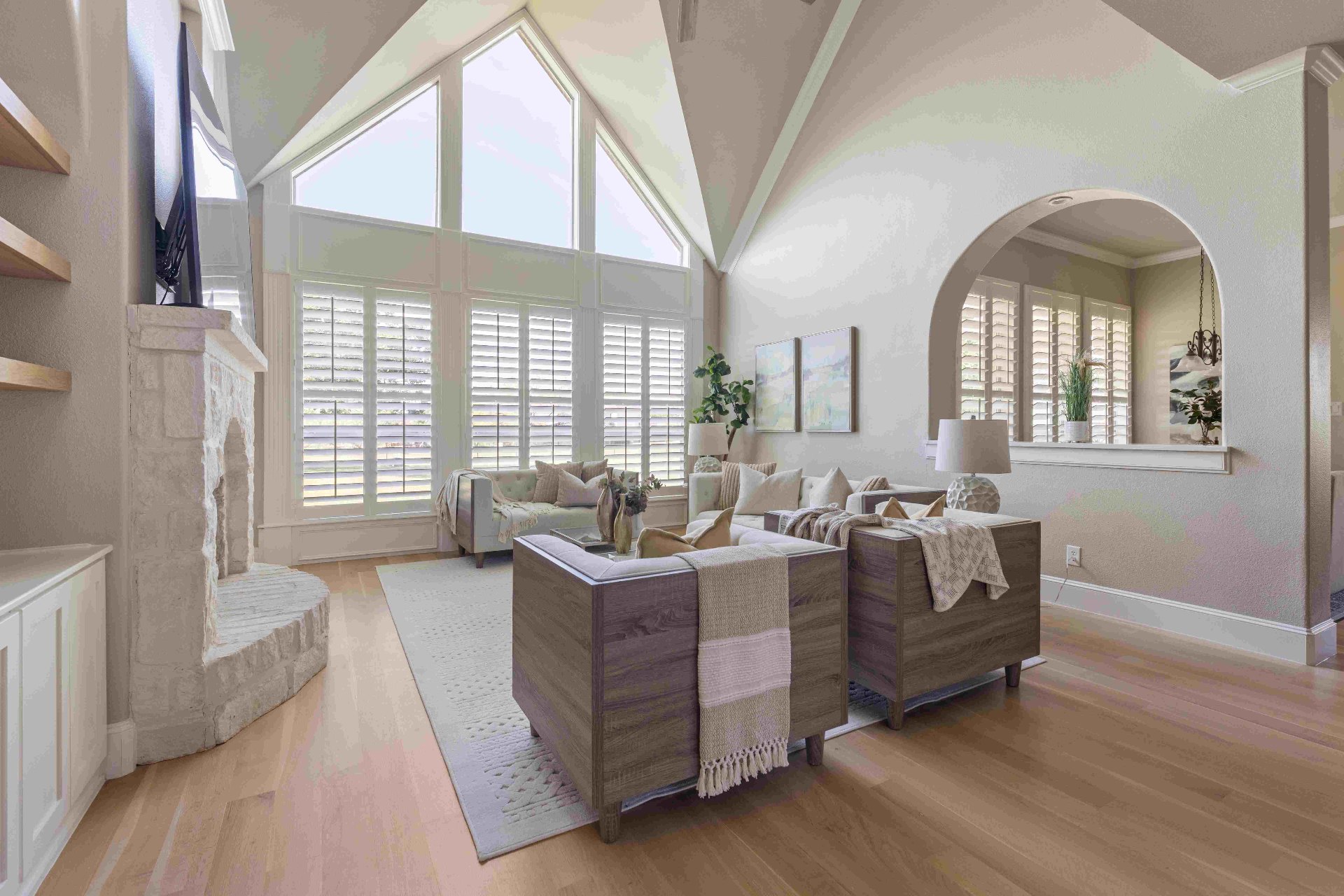 Vaulted living room with floor-to-ceiling windows, stone fireplace, and arched pass-through