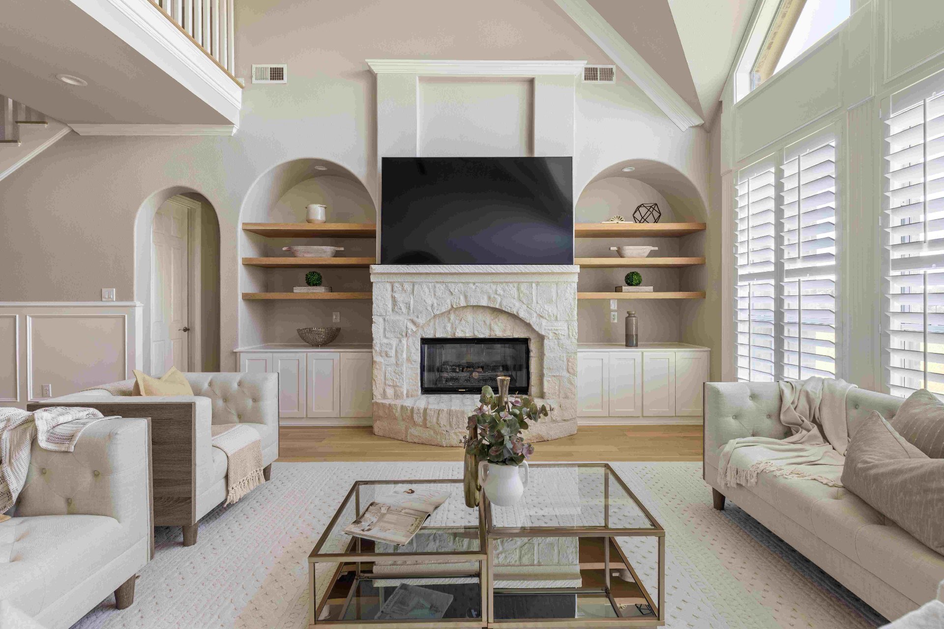 Living room with stone fireplace, built-in arched niches, floating oak shelves, and mounted TV
