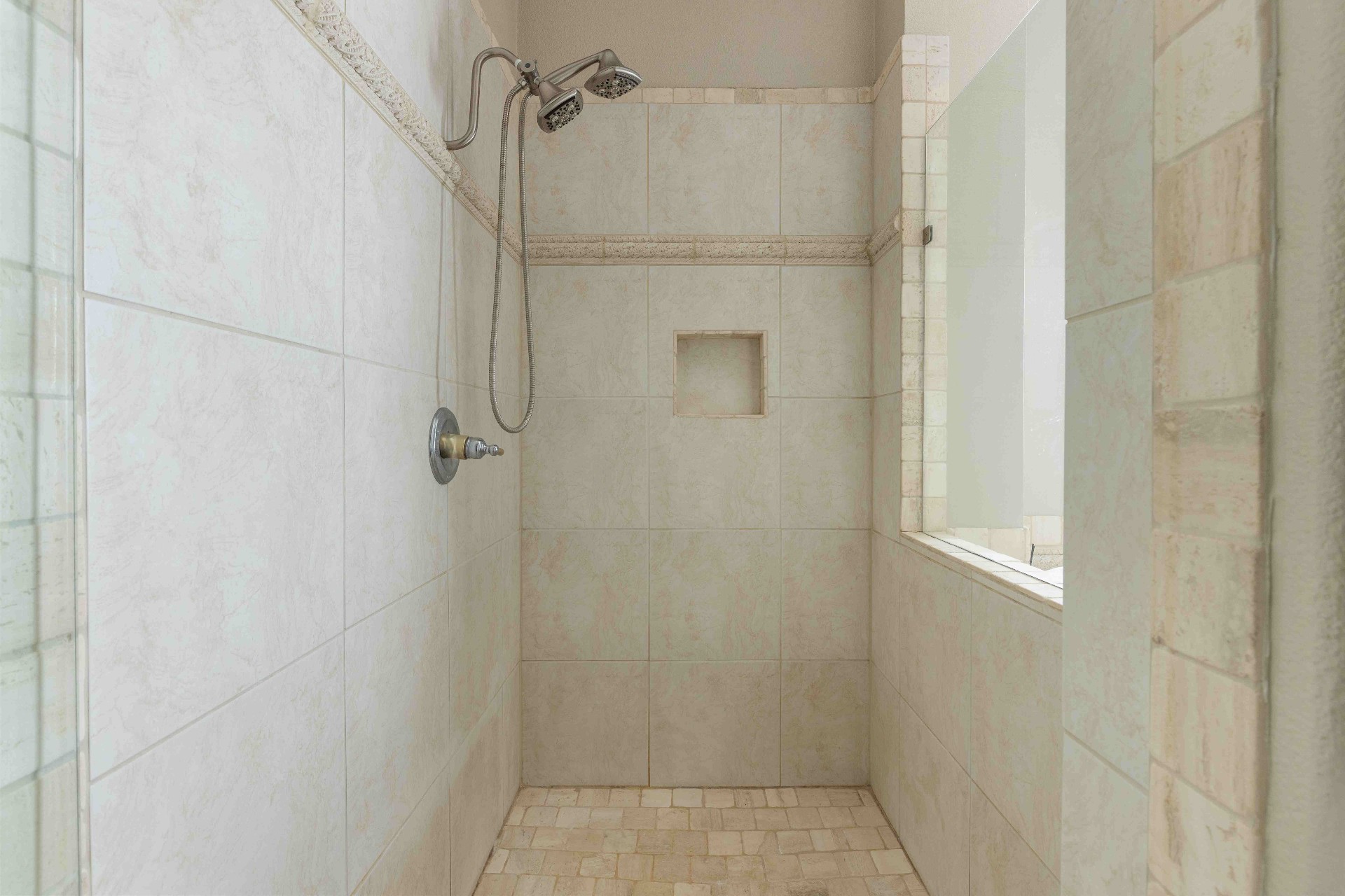 Walk-in primary shower with travertine tile and dual shower heads