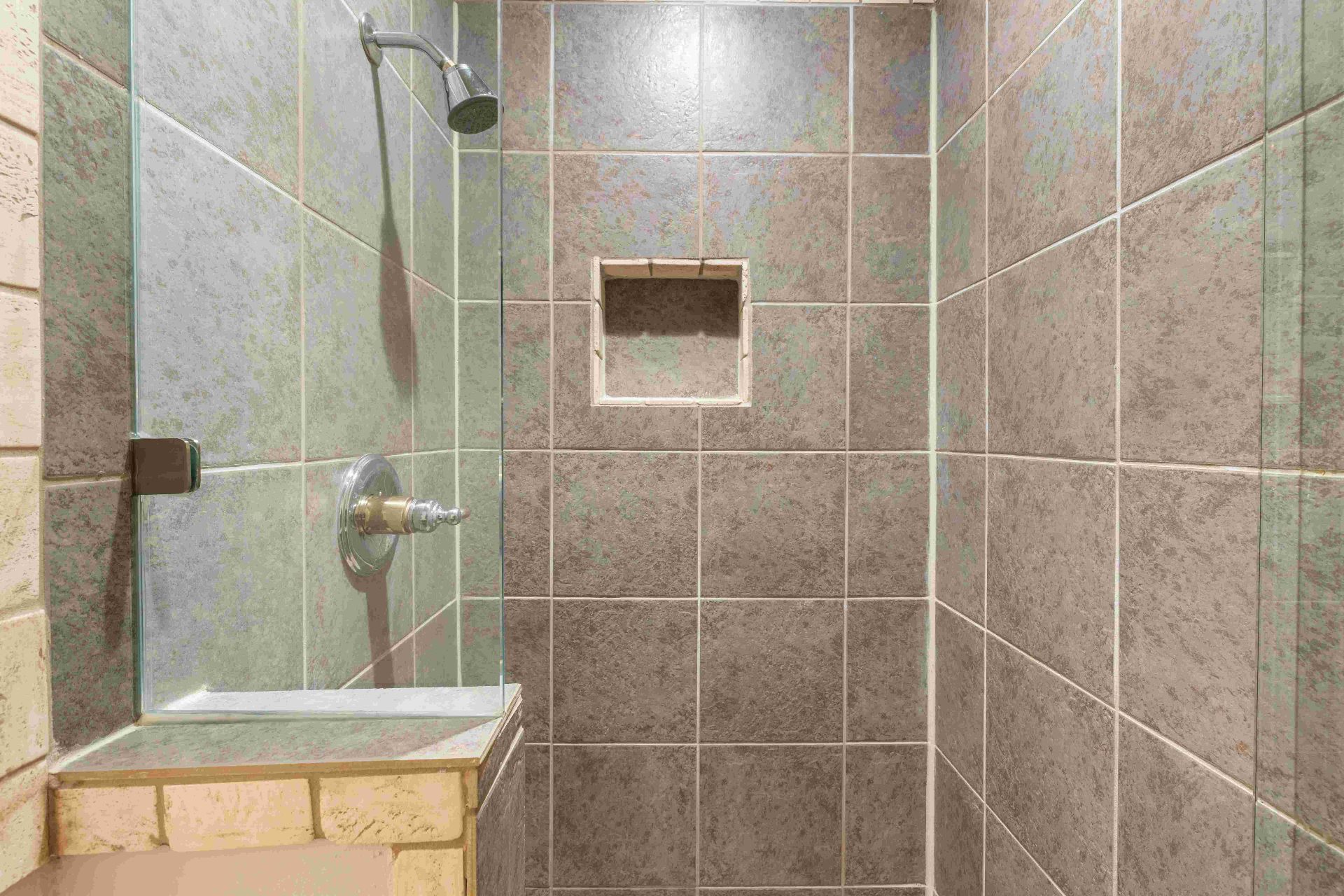 Secondary bath walk-in shower with travertine tile, niche, and glass partition