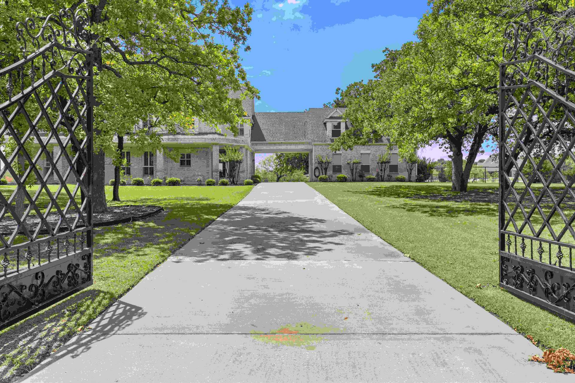 Open wrought iron gates framing the long driveway to the brick estate